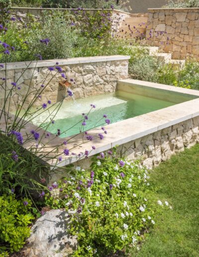 Bassin en pierre semi-enterré avec eau turquoise et plantations autour