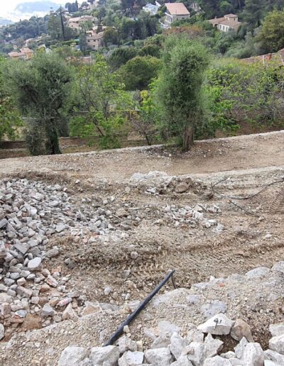 View of a terraced landscape construction site with piles of rubble, worked soil and olive trees in the background