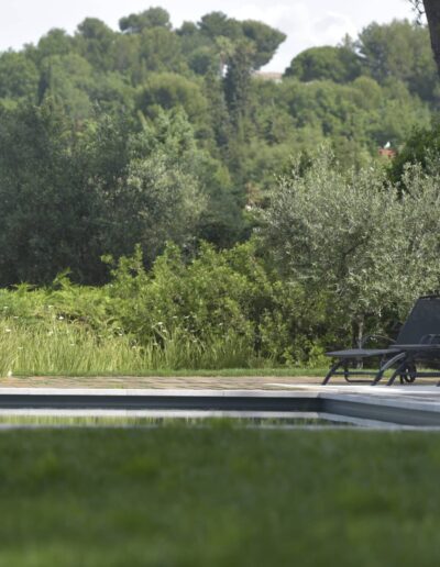 Piscine entourée de chaises longues, d’arbustes et de verdure estivale