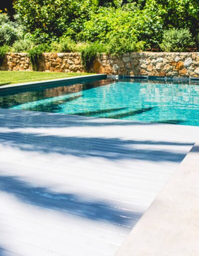 Partially closed automatic pool cover with wooden deck and garden in the background