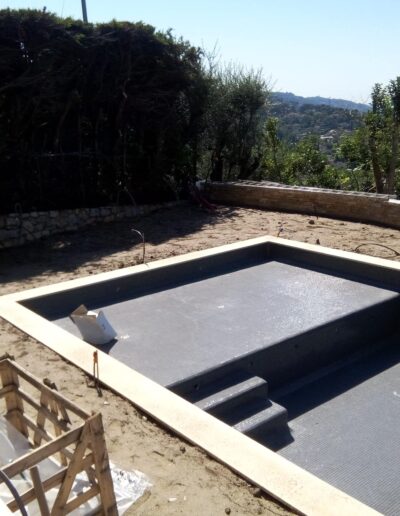 Swimming pool under construction with earthworks and stone walls in the background.