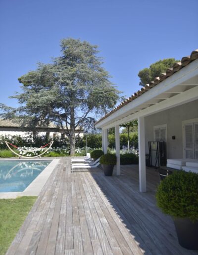 Wooden pool deck with white loungers and a large cedar tree in the landscaped garden background