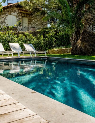Wide view of a pool with white sunbeds, lawn and lush vegetation