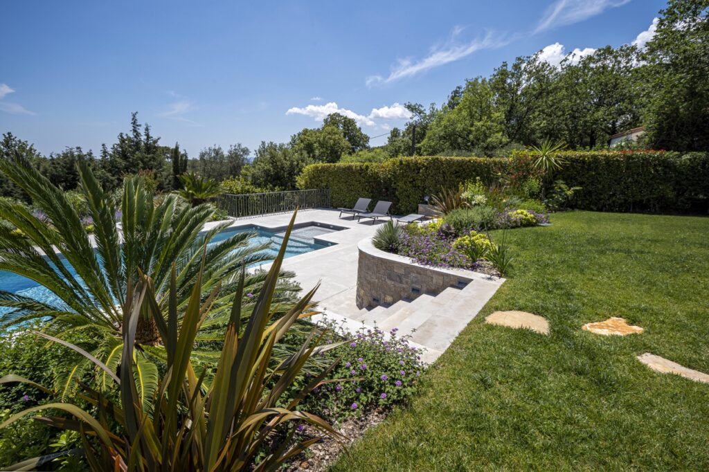 Swimming pool surrounded by Mediterranean vegetation, stone terrace and flower beds