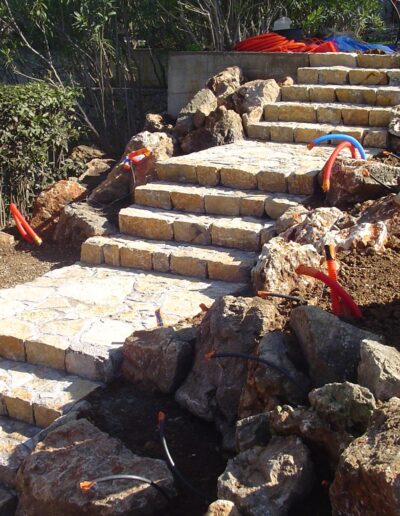 Stone staircase under construction in a garden with rockwork and visible utility conduits