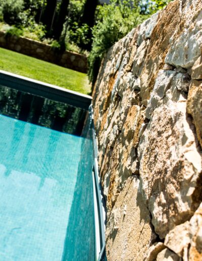 Close-up of a stone wall next to a tiled pool and lush garden