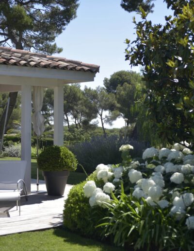 Covered terrace with white lounge chairs and a bed of white hydrangeas in a Mediterranean garden
