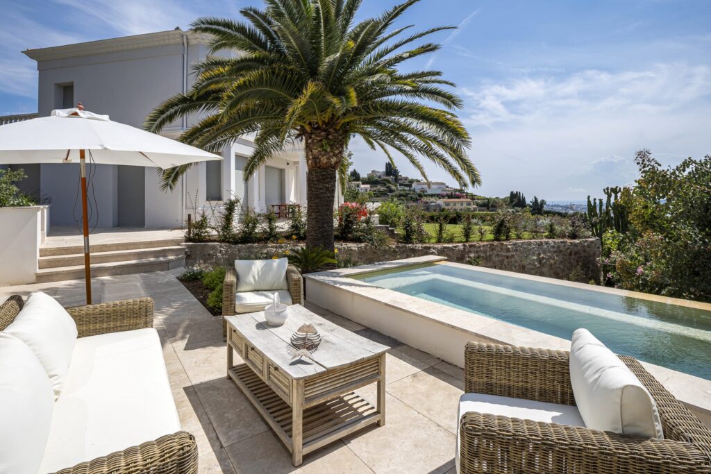 Terrasse aménagée avec mobilier extérieur, palmiers et bassin rectangulaire surplombant le paysage