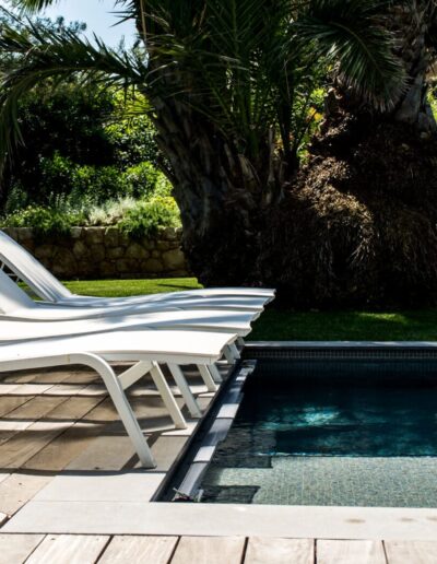 Alignement de transats blancs au bord d’une piscine entourée de végétation méditerranéenne