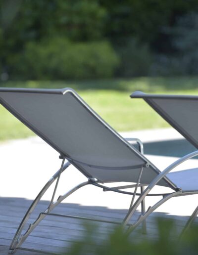 Deux transats modernes installés sur une terrasse en bois au bord d’une piscine