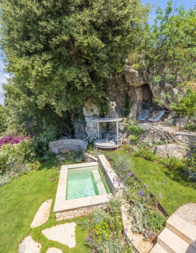 Vue en hauteur du bassin en pierre et des plantations dans le jardin de la villa Hinn