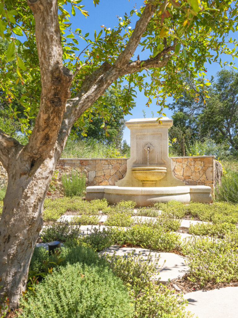 Stone fountain built against a stone wall, part of a landscape project by Adonis Paysages