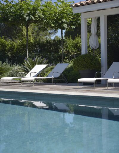 Modern white sun loungers on a wooden deck with a green hedge in the background