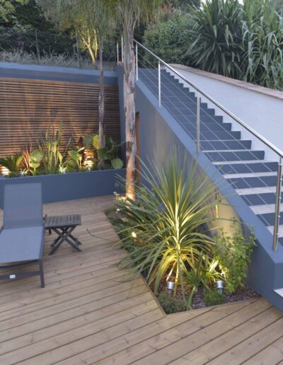 Wooden deck with modern staircase and illuminated garden plants at dusk